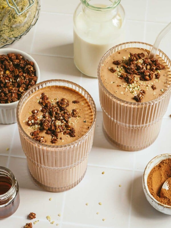 Image shows 2 glasses of creamy and thick silken tofu smoothie blended with chocolate and topped with chocolate granola toppings.