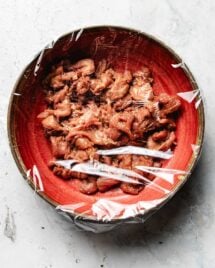 Image shows a bowl of thinly sliced pork velveted with pork stir fry marinade, covered in a red bowl.