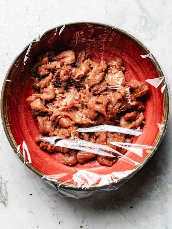 Image shows a bowl of thinly sliced pork velveted with pork stir fry marinade, covered in a red bowl.