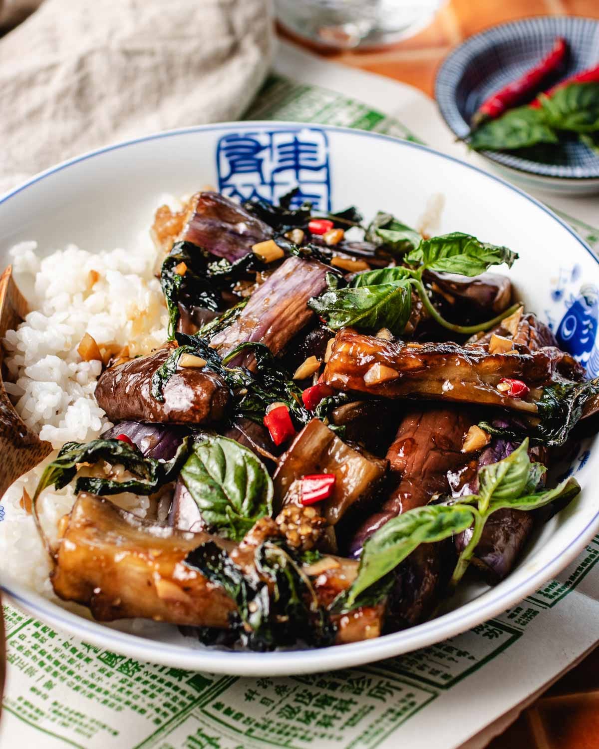 A side close shot shows buttery soft Thai eggplants coated with sweet basil sauce in a bowl.