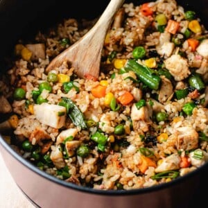 A close shot image shows crisp rice grains air fried in an air fryer basket with chicken and vegetables.