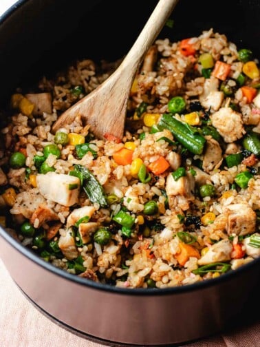 A close shot image shows crisp rice grains air fried in an air fryer basket with chicken and vegetables.