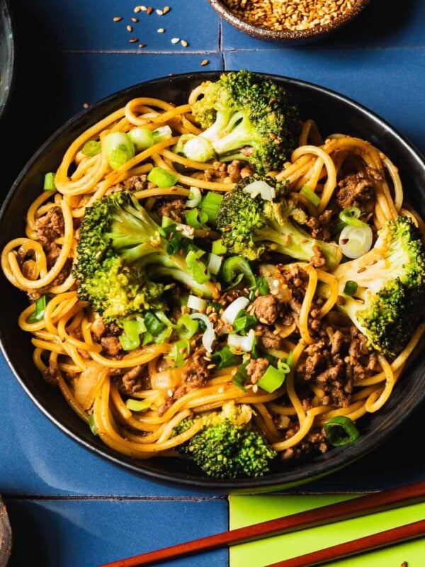 Image shows a plate of ground beef and noodle stir fried with broccoli. Served with chopsticks on the side.