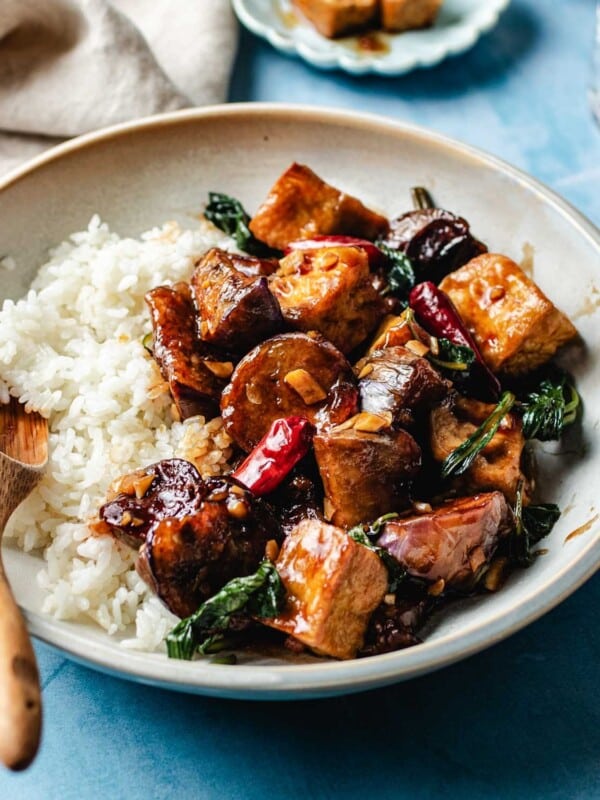 A side shot image shows buttery soft eggplants stir fried with tofu puffs with basil, chili, and garlic sauce.