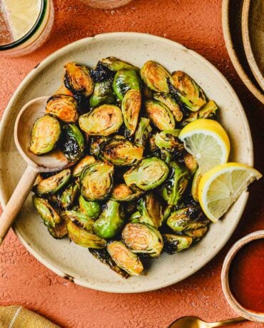 An overhead image shows crispy brussel sprouts tossed in honey sriracha sauce, served on a white color plate.