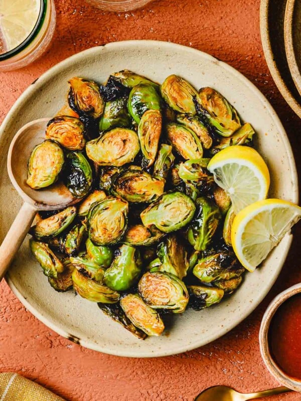 An overhead image shows crispy brussel sprouts tossed in honey sriracha sauce, served on a white color plate.