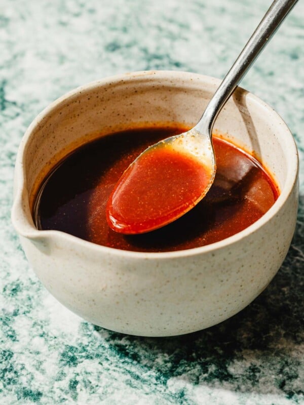 Image shows honey sriracha sauce with smooth and glossy texture in a white ceramic bowl with a spoon.