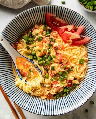 An overhead image shows a bowl of tomato ramen with rich tomato broth served in a blue and white color Japanese ramen bowl.