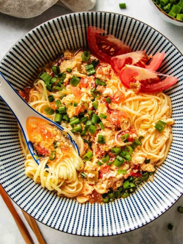 An overhead image shows a bowl of tomato ramen with rich tomato broth served in a blue and white color Japanese ramen bowl.