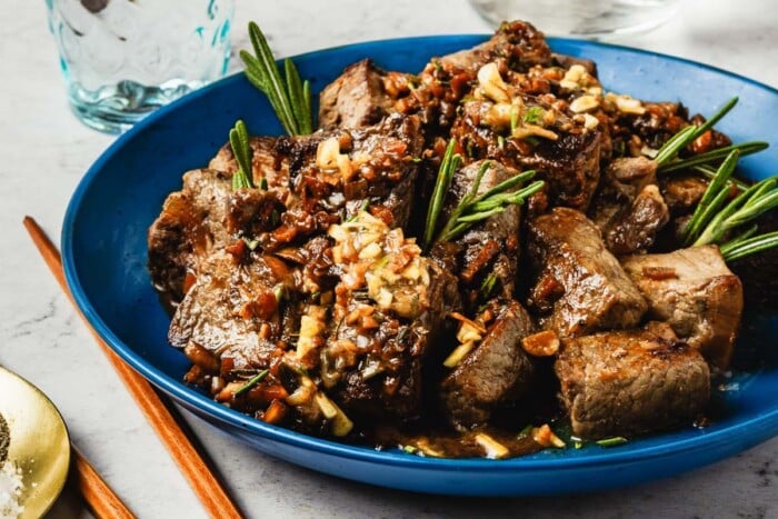 Image shows seared beef cubes with garlic and rosemary, served on a plate.