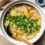 Recipe image shows napa cabbage soup with egg ribbons and scallions served in a white color clay pot.