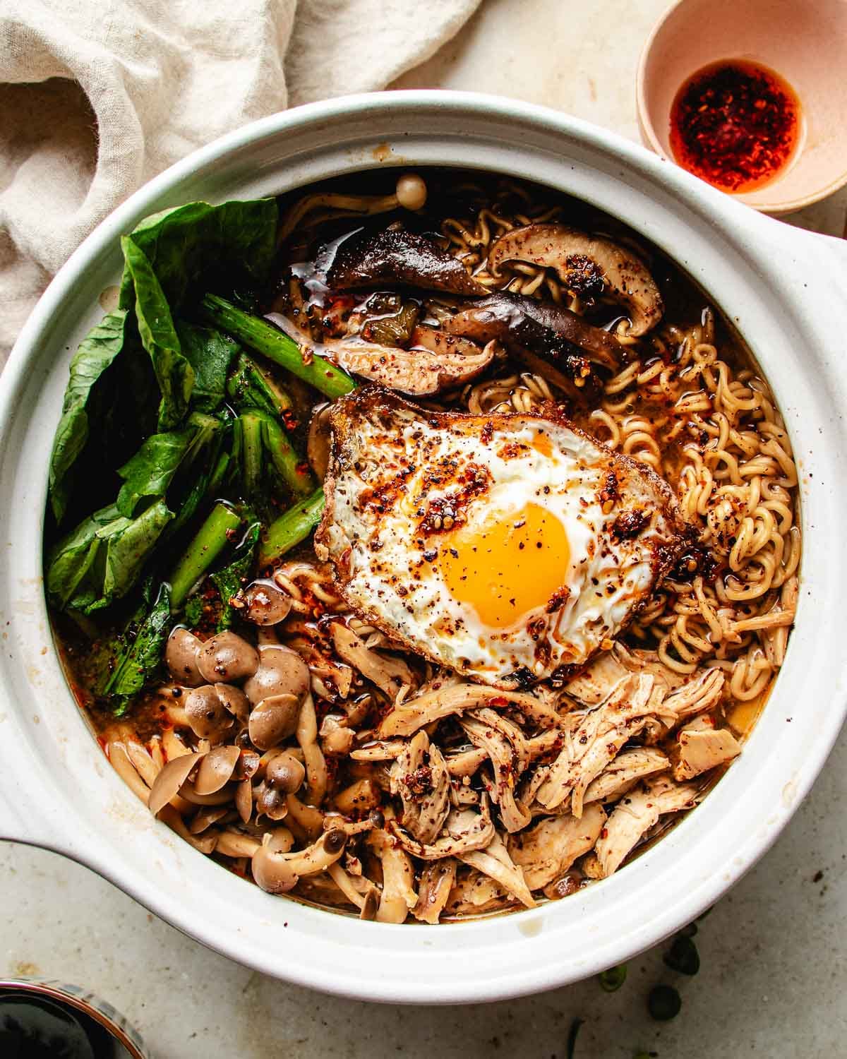 Feature overhead image shows spicy chicken noodle soup in a donabe soup pot with ramen noodles, cooked chicken, mushrooms, and vegetable, plus a fried egg on top.