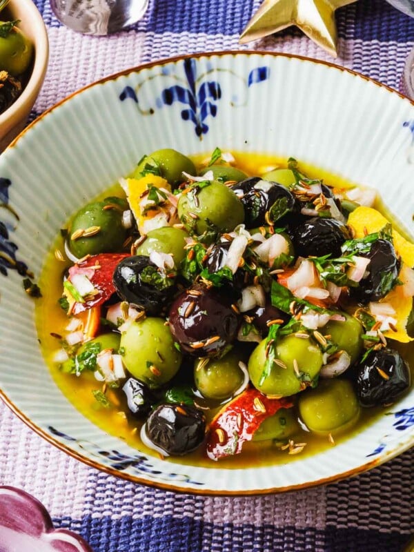 Feature image shows a close shot of blue white color bowl with homemade marinated olives inside.