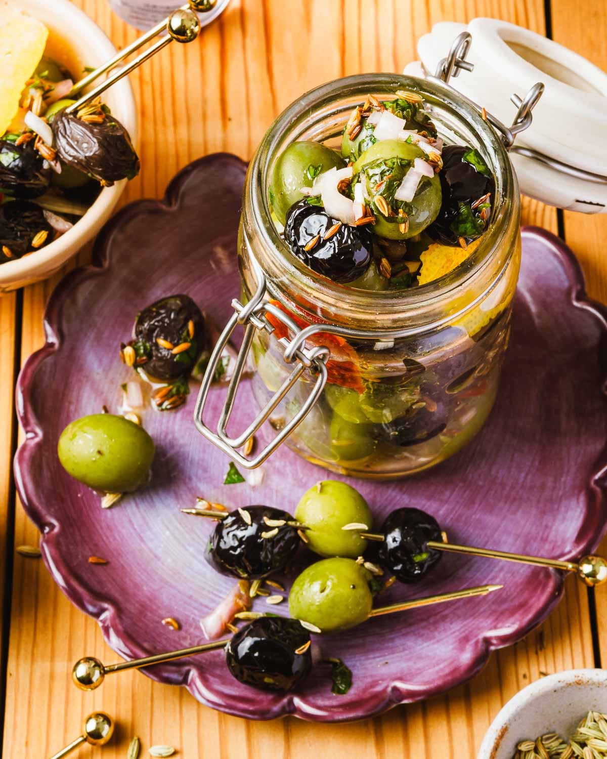 A side image shows marinated olives in a glass jar with some on the side over a purple plate.