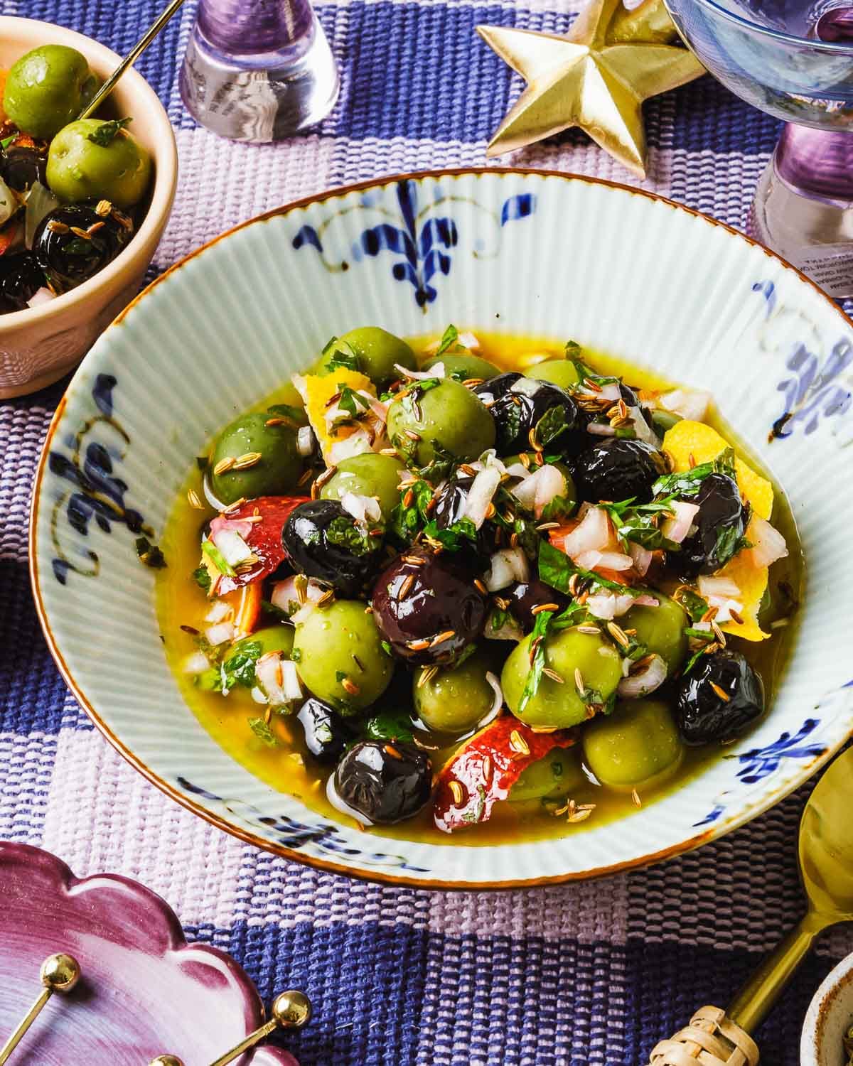 Image shows a bowl of marinated green and black olives, marinated in olive oil, spices, and herbs.