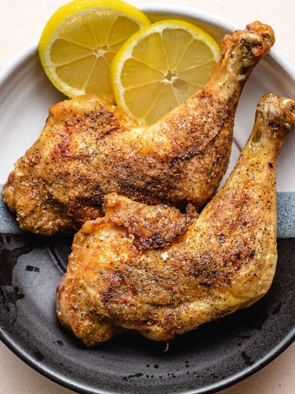 An overhead close shot shows crispy skin leg quarters air fried and served with lemon on the side.