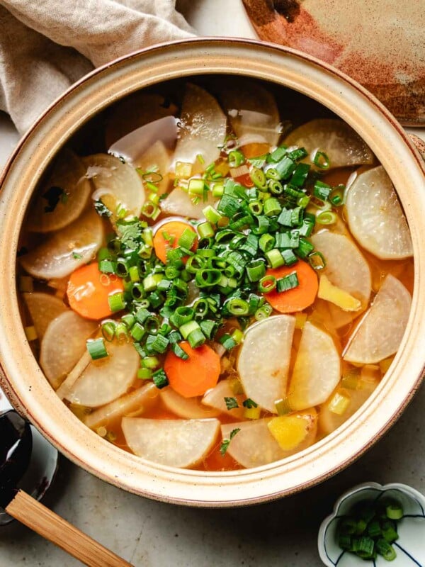 Feature image shows a big clay pot filled with daikon radish soup with clear chicken broth, sliced carrots and scallion garnish over.