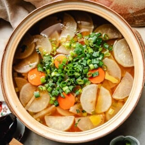 Recipe image for daikon radish soup in a big clay soup pot with slices of daikon and some carrots simmered in chicken broth.