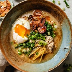 Recipe image shows the creamy texture of Asian chicken rice soup with poached egg, garlic chips, and toasted sesame oil.