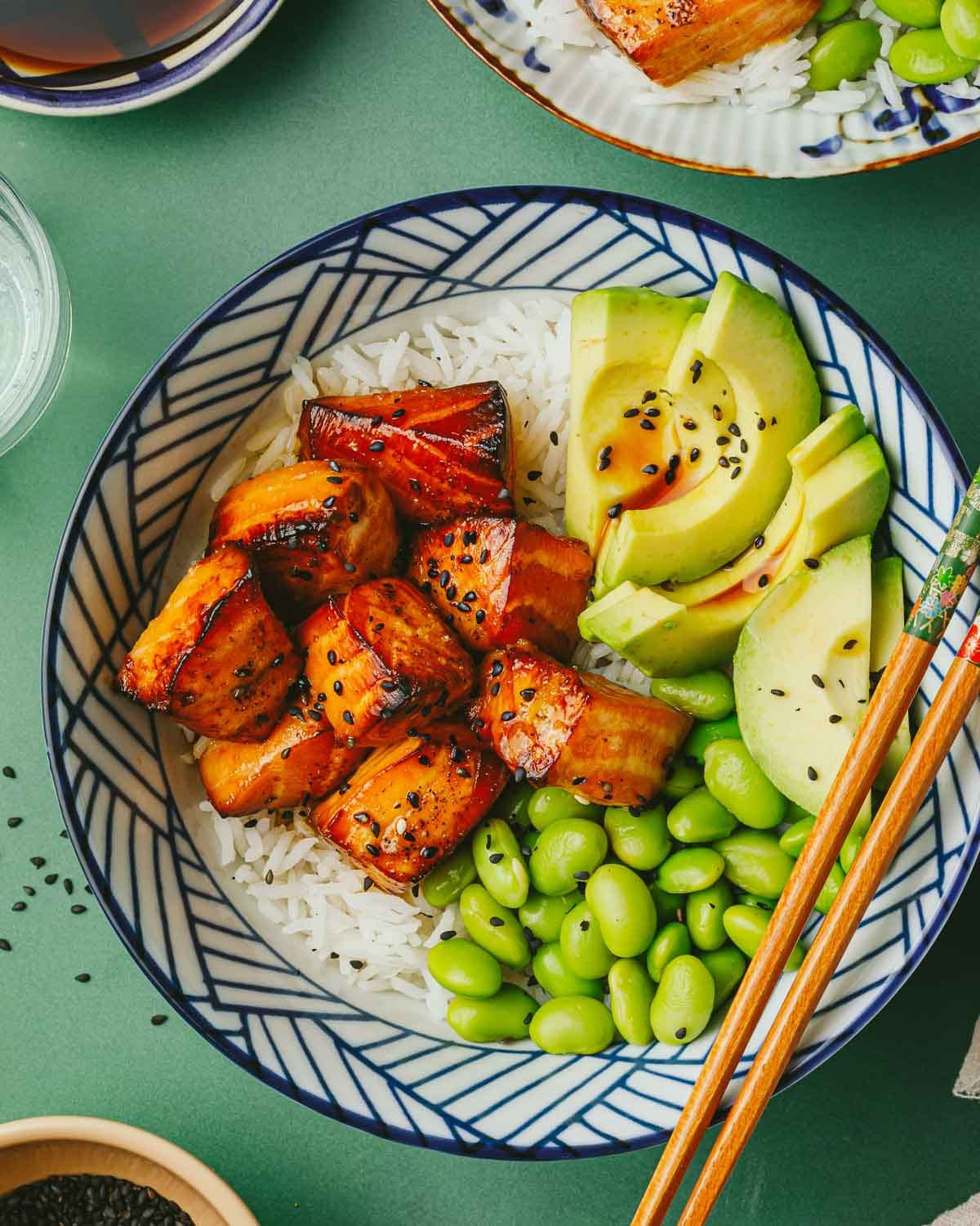 Feature overhead image shows a bowl of teriyaki salmon bites with teriyaki sauce served in a rice bowl.