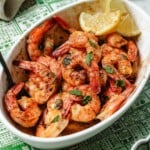 Recipe image shows a plate of air fryer frozen shrimp made in a baking dish inside of air fryer basket.