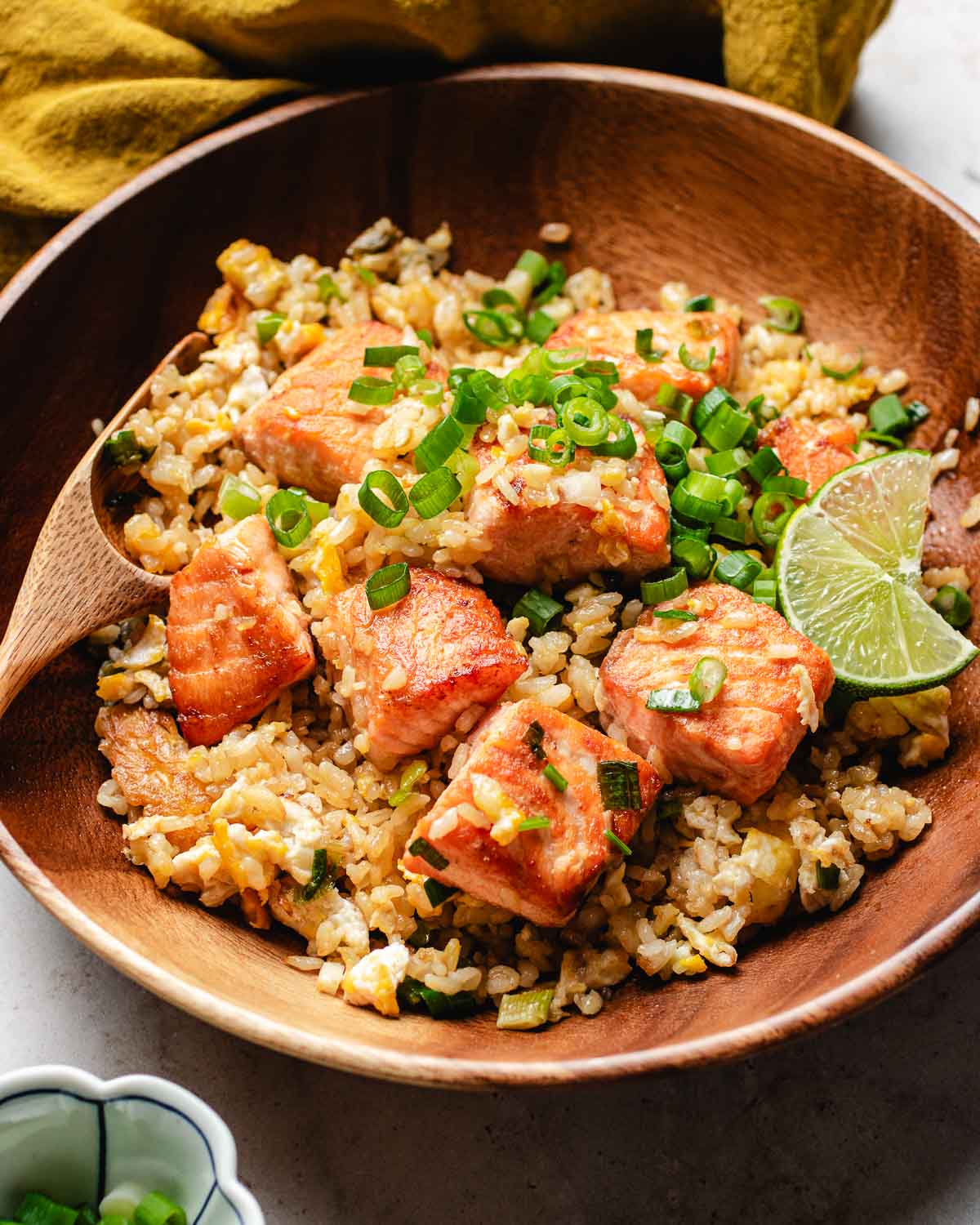 A side close shot shows juicy salmon stir fried with rice and garnishes with lime and Thai chili sauce.