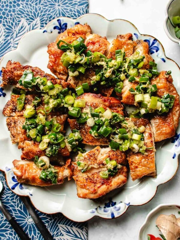 Feature image shows crispy chicken thighs with scallion oil drizzled on top, served on a blue white color plate.