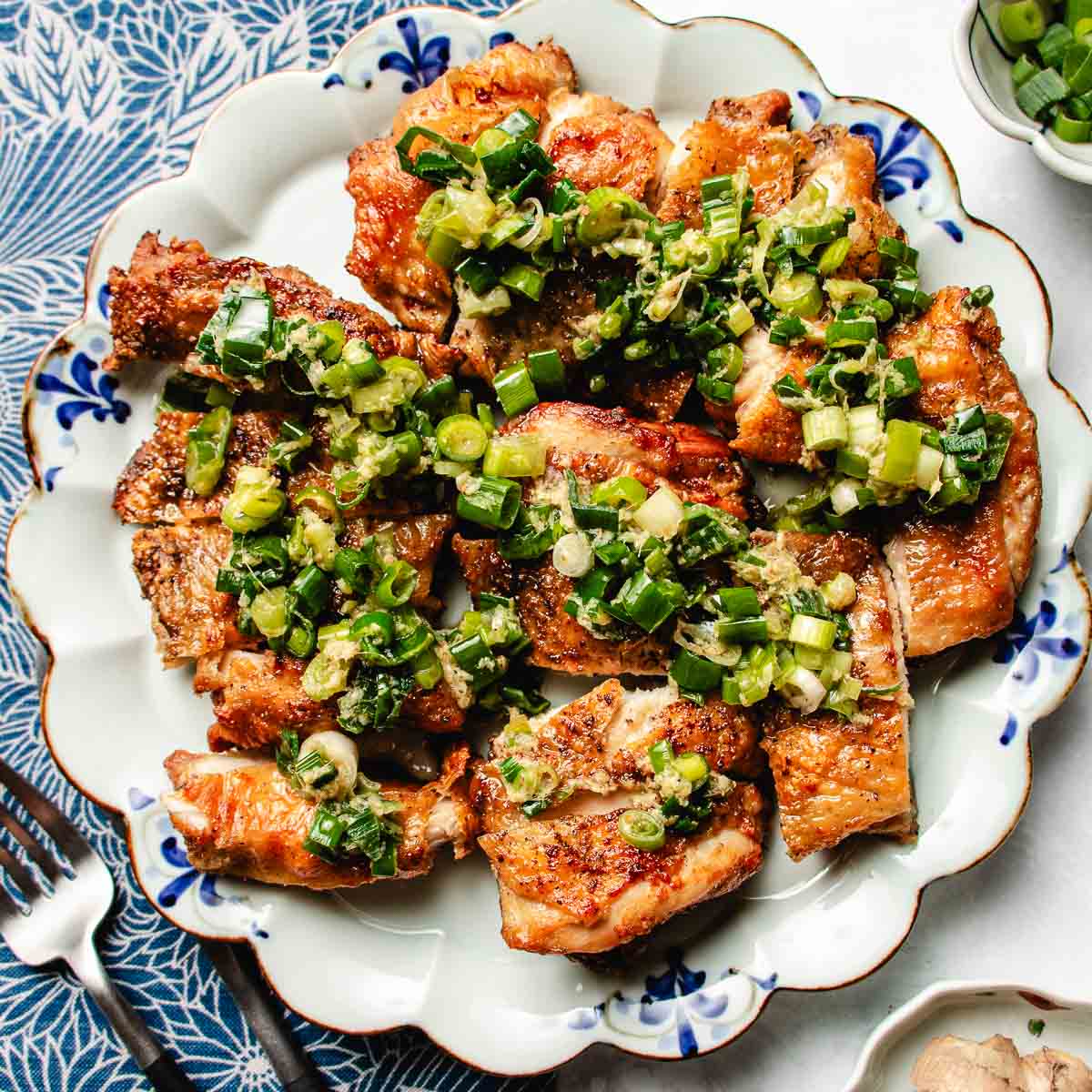 Recipe image shows scallion chicken with crispy skin and loads of ginger scallion on top and served on a blue white color plate.