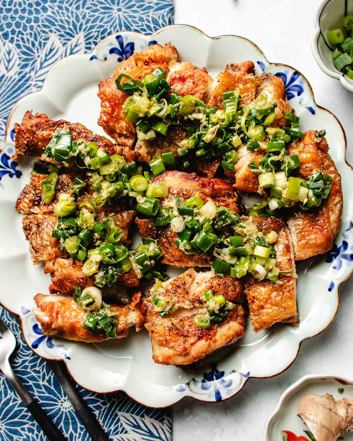 Feature image shows crispy chicken thighs with scallion oil drizzled on top, served on a blue white color plate.