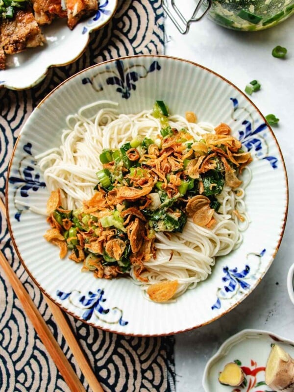 Feature image shows a bowl of noodles seasoned with scallion oil and with crispy shallots on top, served in a blue white color Asian noodle bowl.