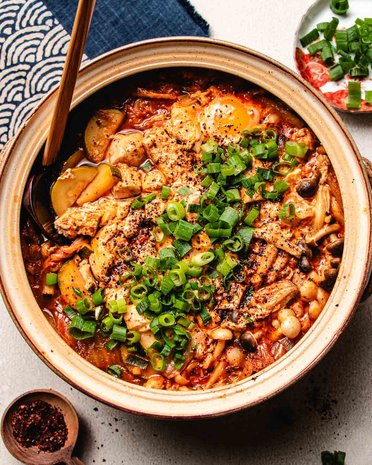 Feature overhead image shows silken tofu stewed with kimchi and vegetables in a big donabe soup pot.