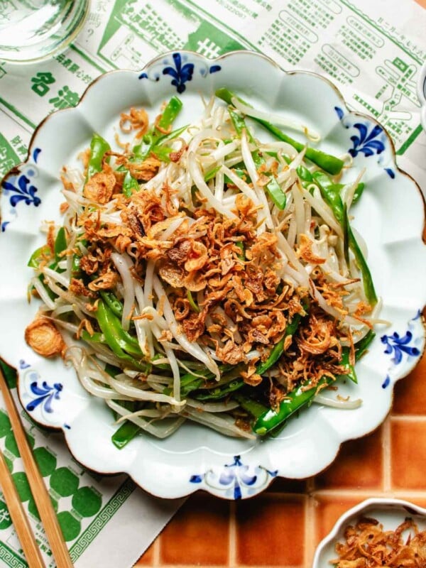 Feature overhead image shows a plate of crisp stir fried bean sprouts topped with crispy shallots and thin sliced snow peas, Taiwanese style.