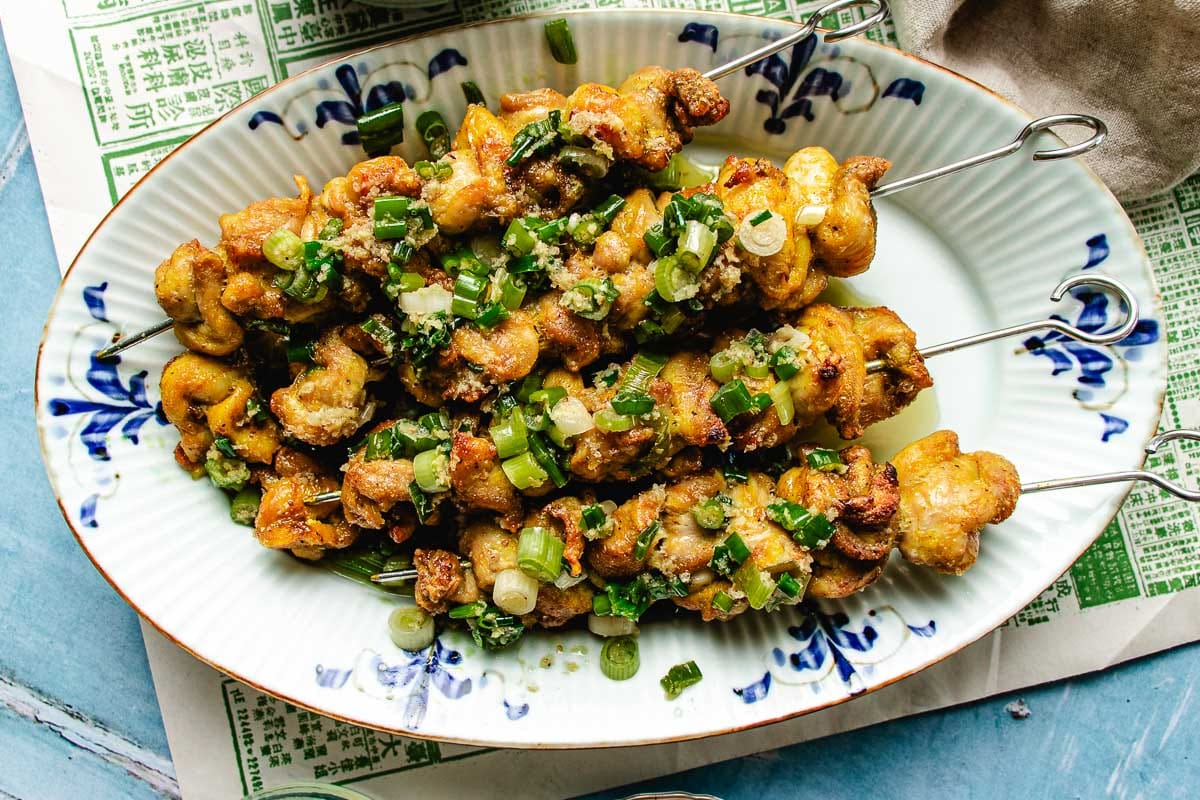 A horizontal feature image with chicken skewers and ginger scallion sauce on top.