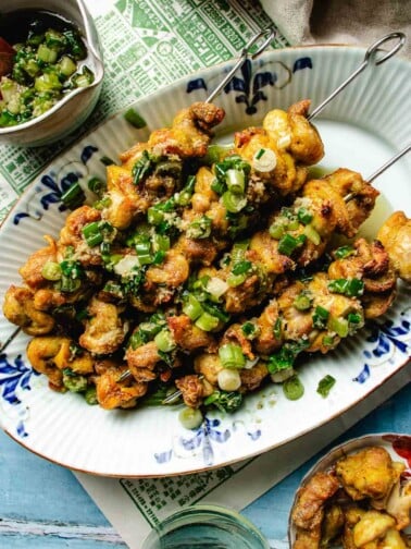 Feature image shows air fried chicken kabobs with ginger scallion sauce on top, served in a blue white color plate.