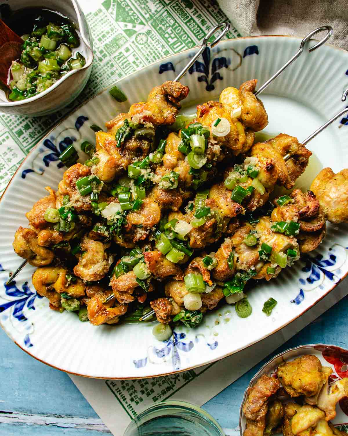 Feature image shows air fried chicken kabobs with ginger scallion sauce on top, served in a blue white color plate.