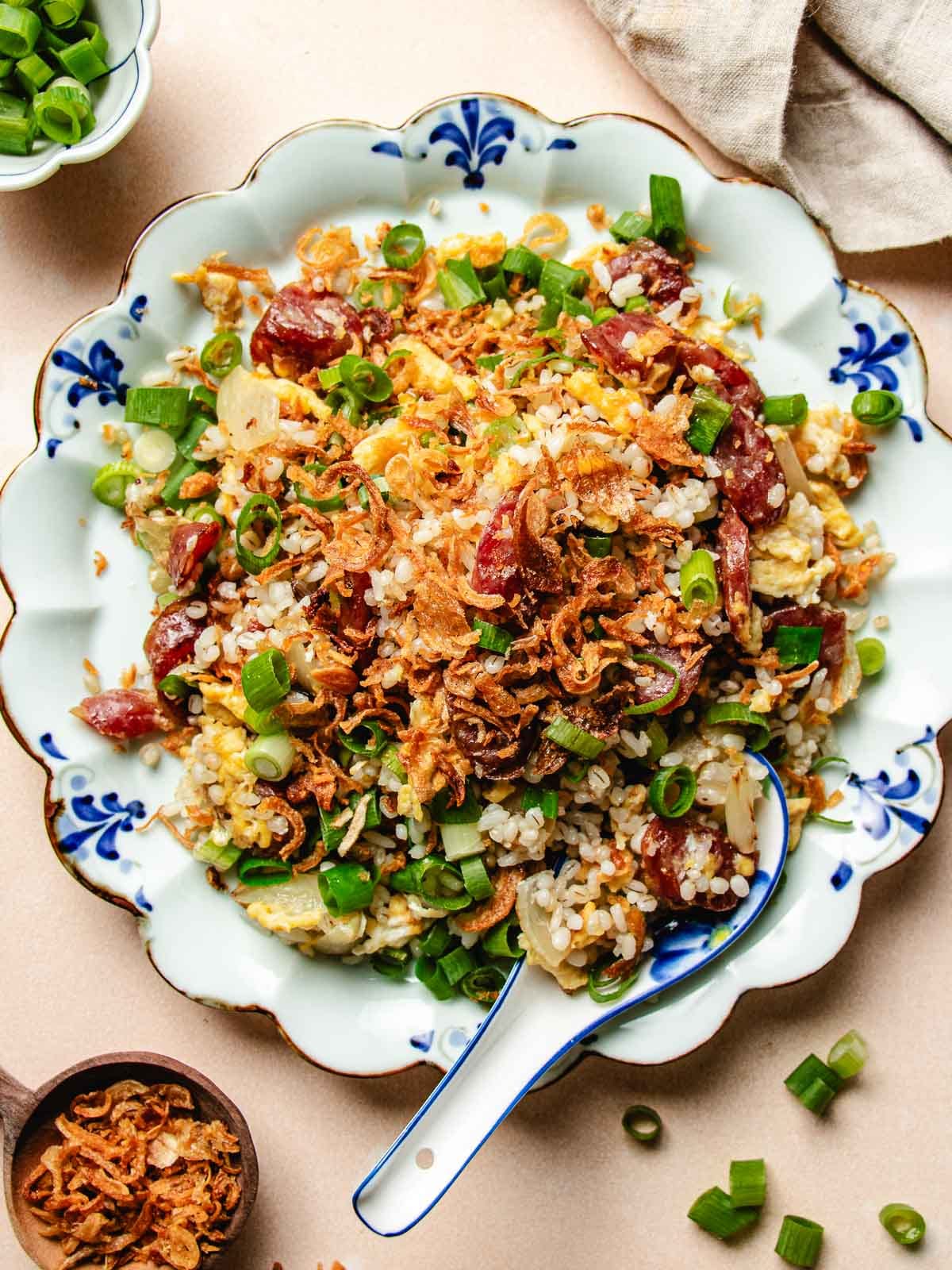 Overhead feature image shows a plate of golden crisp fried rice with Chinese sausage served in a blue white color plate.
