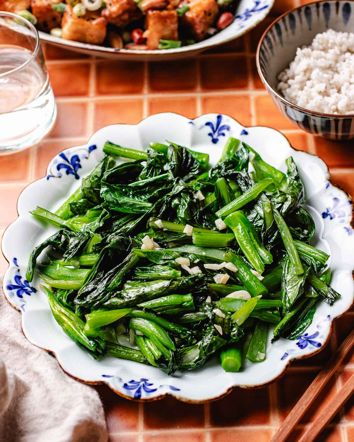 A side shot shows a plate of stir fried yu choy, served with rice and tofu side dishes on the side.