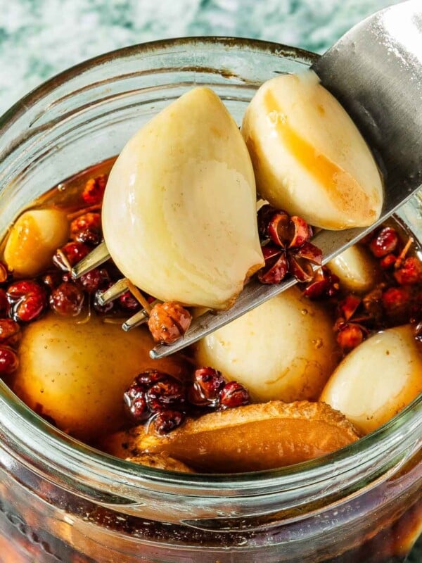 Feature image shows a close shot of pickled garlic cloves in a sichuan style ginger peppercorn brine.