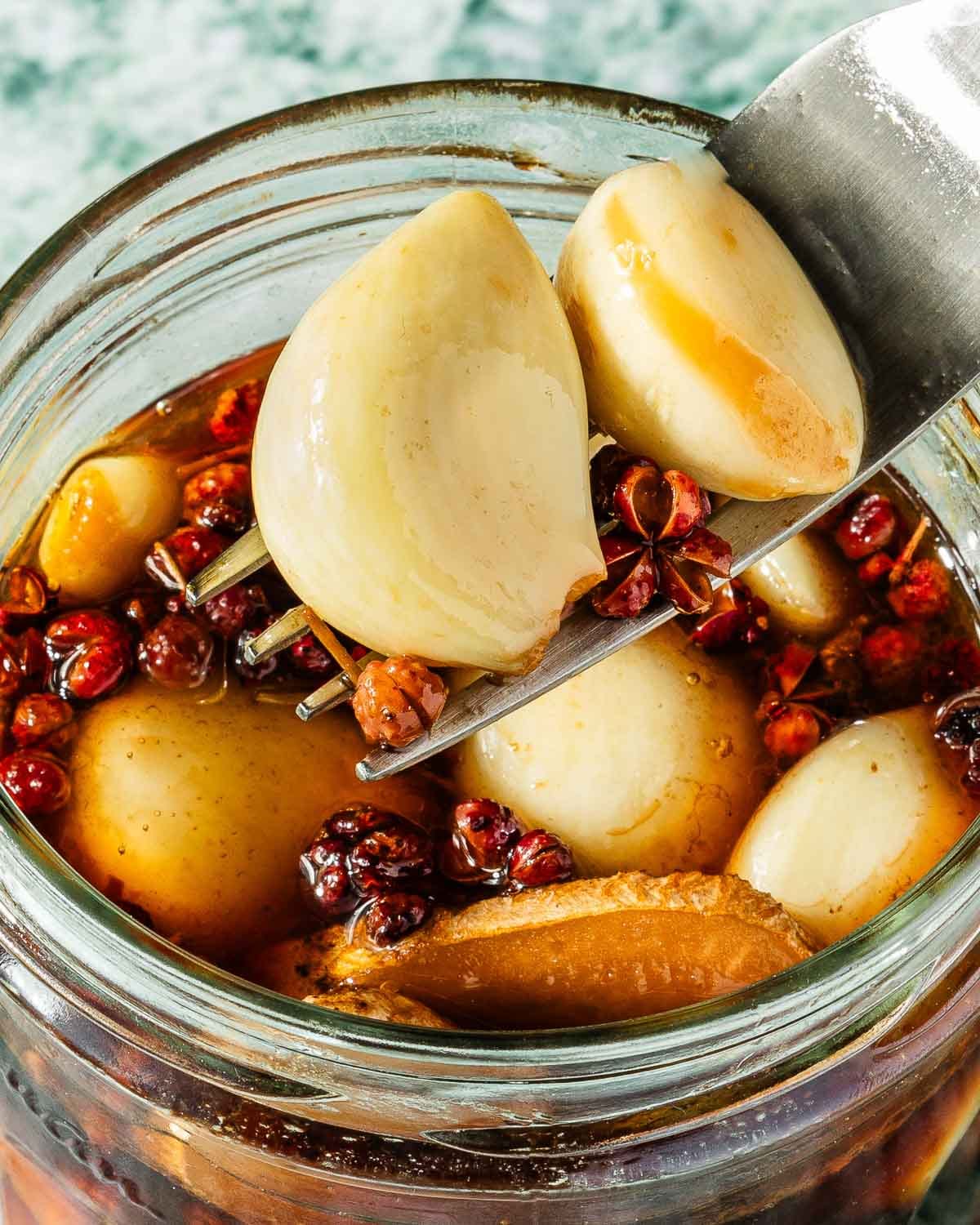 Feature image shows a close shot of pickled garlic cloves in a sichuan style ginger peppercorn brine.