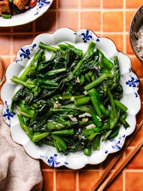 Photo shows a plate of stir fried choy sum with garlic, served over a blue white color plate with chopsticks on the side.