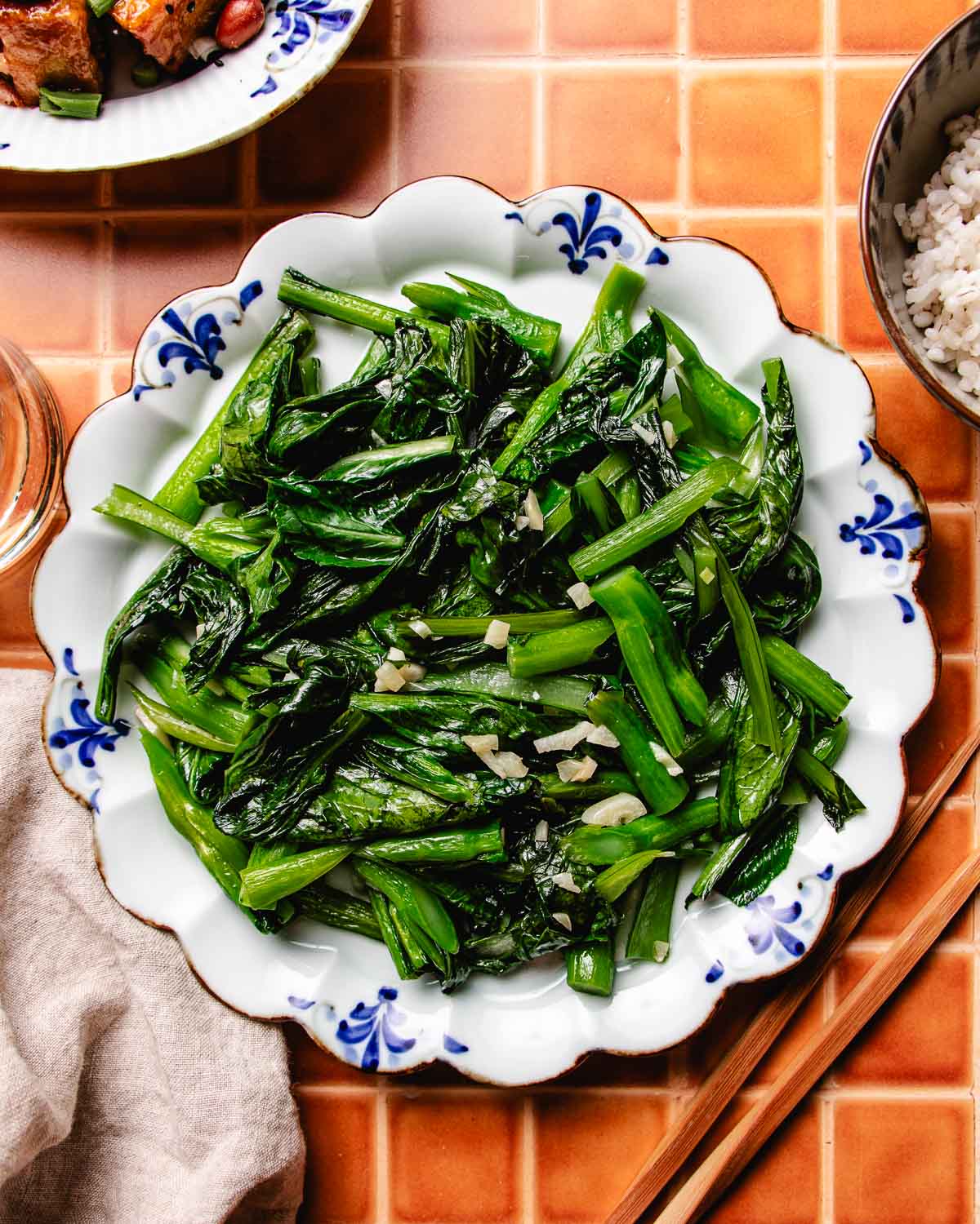 Photo shows a plate of stir fried choy sum with garlic, served over a blue white color plate with chopsticks on the side.