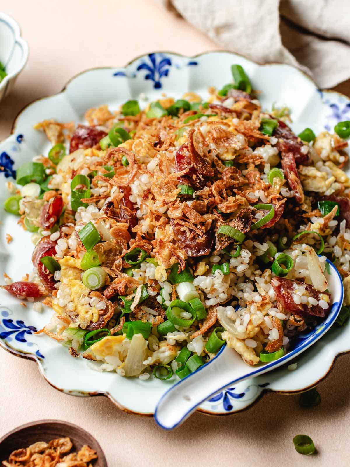 A side close shot shows Chinese sausage in fried rice served over a white blue color plate.