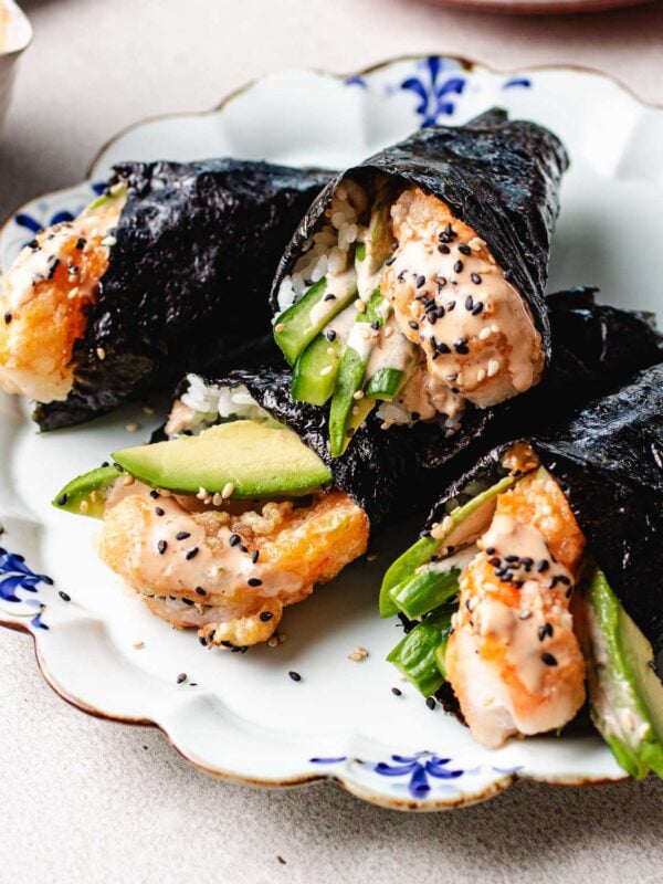 Feature image shows crispy bang bang shrimp wrapped in nori wraps into hand rolls with cucumber, avocado, and sushi rice.