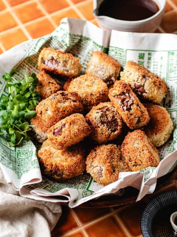 Feature image shows an angle shot with a plate of crispy eggplant mini bites served in a wooden plate with sweet sour dipping sauce on the side.