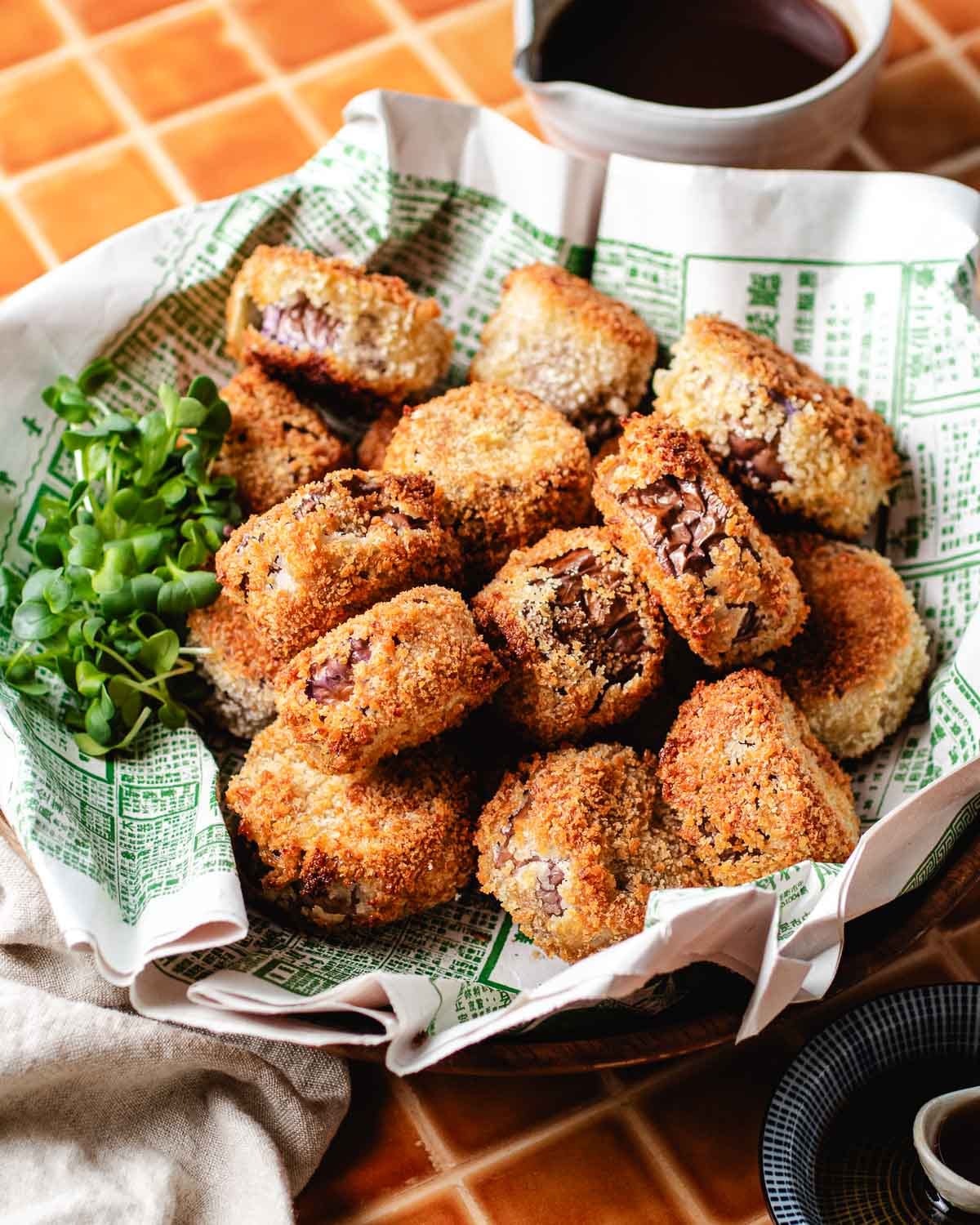 Feature image shows an angle shot with a plate of crispy eggplant mini bites served in a wooden plate with sweet sour dipping sauce on the side.