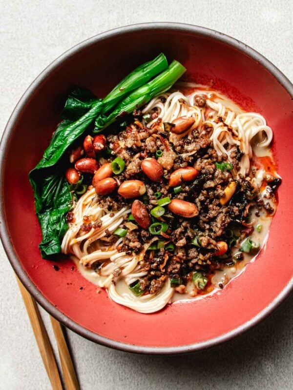 Feature image shows a bowl of dan dan noodles with dan dan sauce served in a red color bowl.