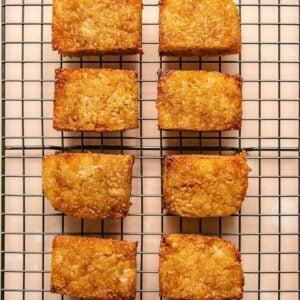 Eight golden brown Crispy Rice squares are arranged in two neat columns on a black wire cooling rack, viewed from above against a neutral background. Perfect for anyone curious about how to make crispy rice treats at home.