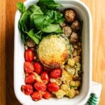 A white dish holds chicken cauliflower casserole, cooked chicken, fresh spinach, roasted cherry tomatoes, white beans, and a baked mound with melted cheese topping—all beautifully arranged on a wooden surface.