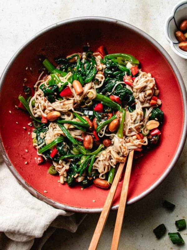 A vibrant cold enoki mushroom salad with spinach, red peppers, and roasted peanuts, tossed in a garlicky, tangy soy-vinegar dressing and served in a deep red bowl.