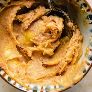 A close-up of creamy miso butter in a bowl with a spoon, highlighting its smooth, thick texture and light brown color.